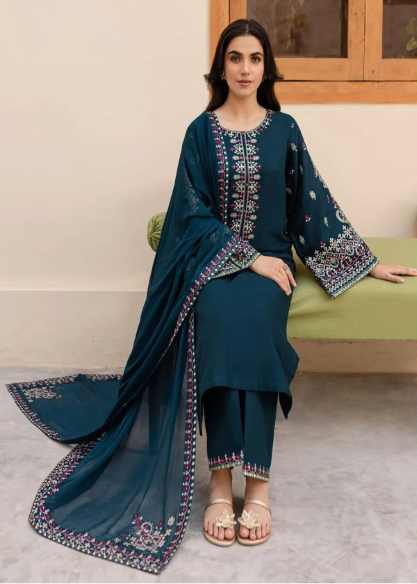 Woman in a blue traditional outfit sitting on a green couch with a neutral wall and window in the background.