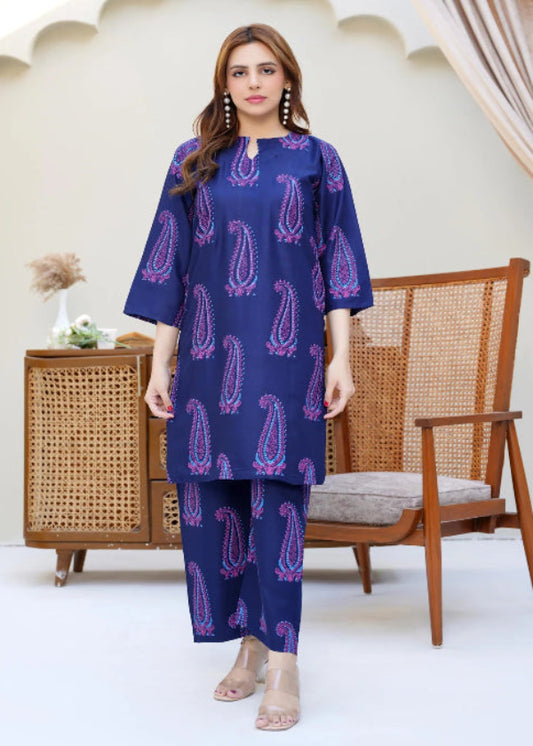 Woman wearing a blue patterned outfit standing in a room with a wooden chair and decorative arches.