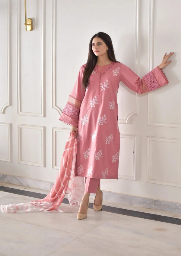 Woman in a pink traditional outfit with white patterns standing against a white wall.